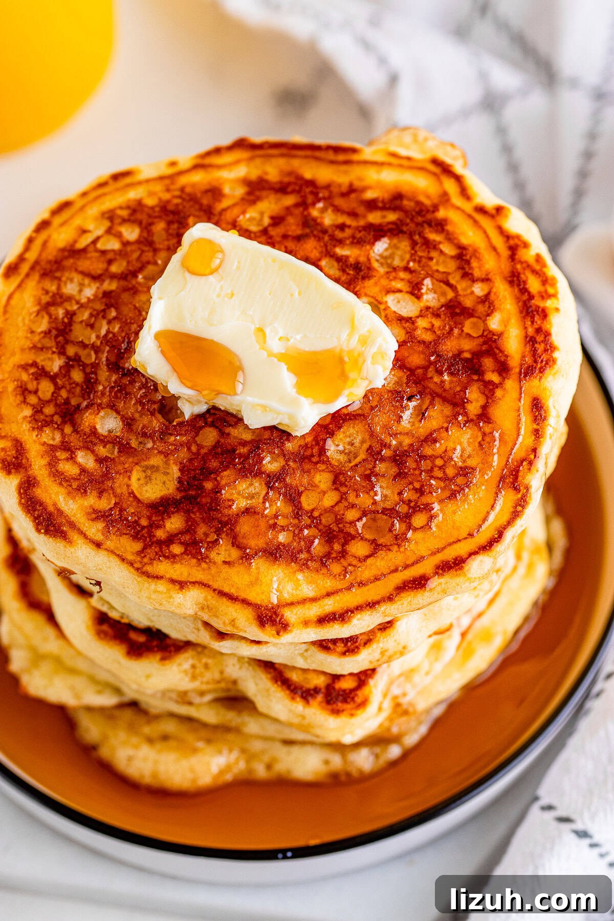 Overhead photo The Best Buttermilk Pancakes stacked showing a pat of butter and syrup.
