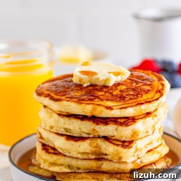 The Best Buttermilk Pancakes stacked on white plate with butter and syrup.