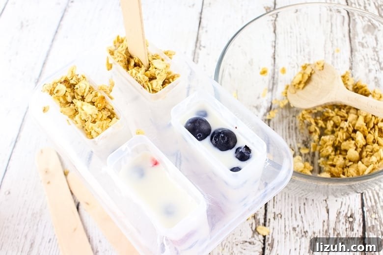 Creamy Yogurt Breakfast Popsicles with Fresh Fruit 5 Popsicle mold filled with yogurt and berries. Some of the molds are topped with granola a well.