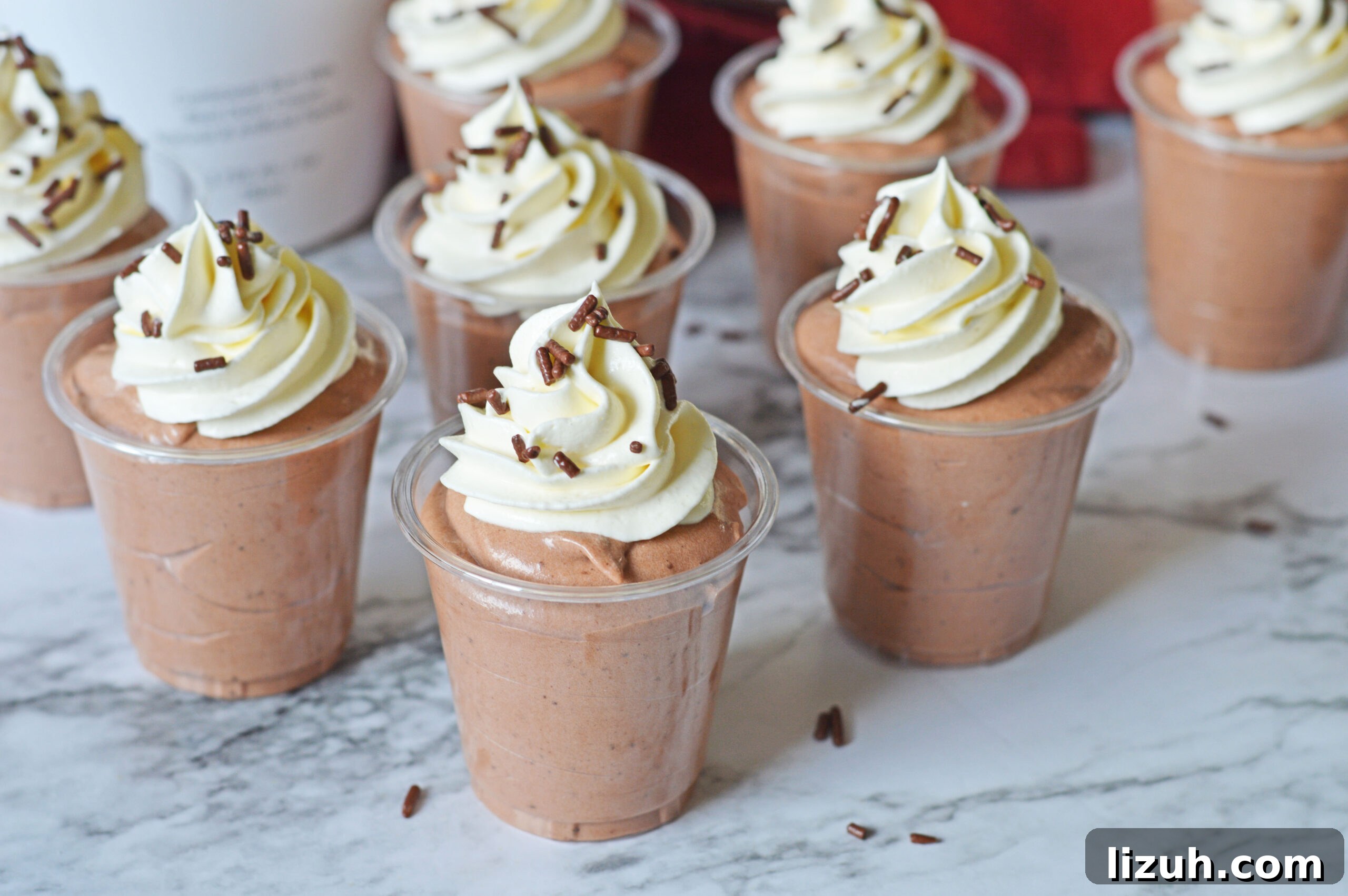 Rumchata pudding shots on a marble table topped with whipped cream and sprinkles