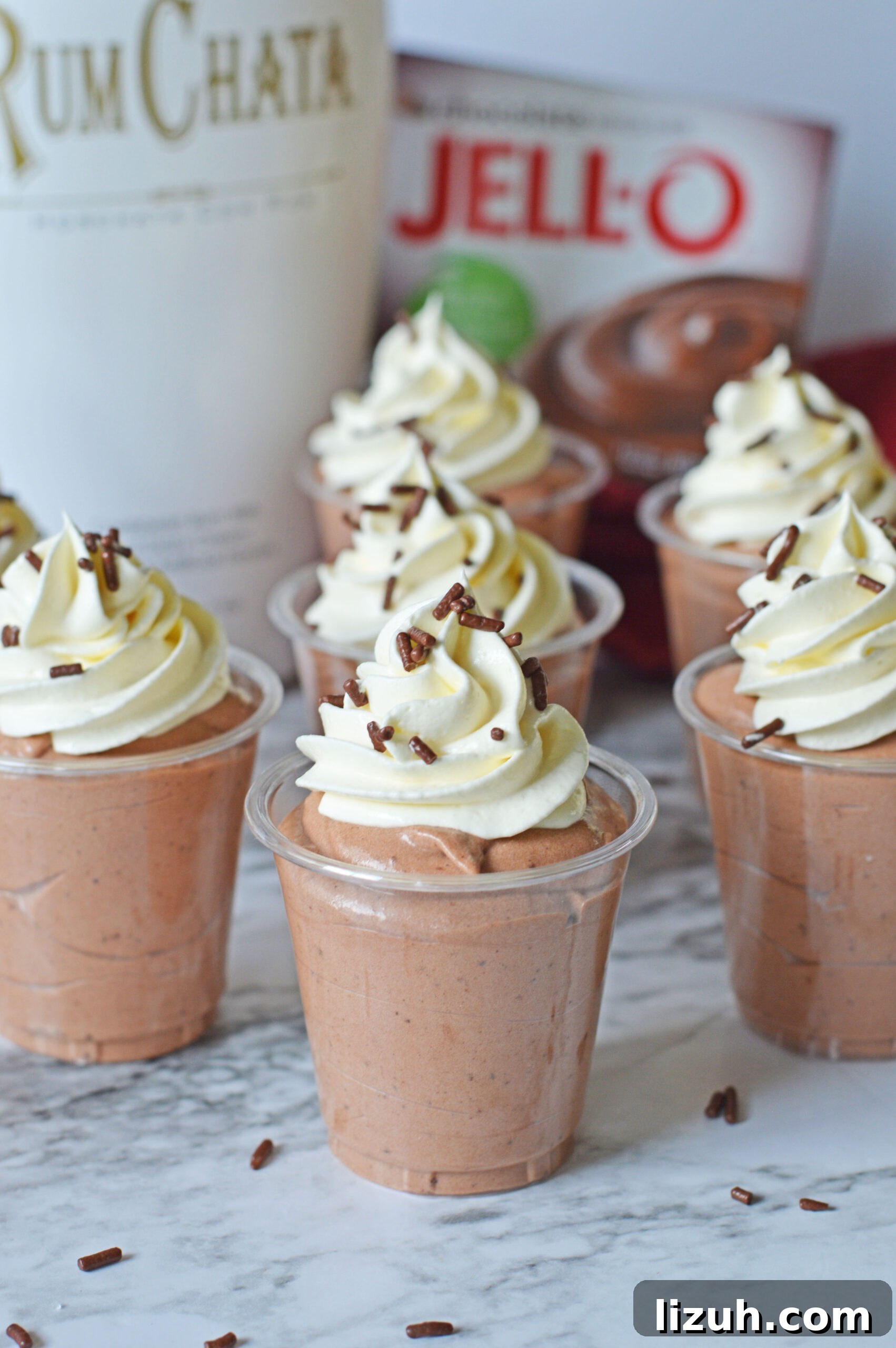 Rumchata pudding shots on a marble table topped with whipped cream and sprinkles