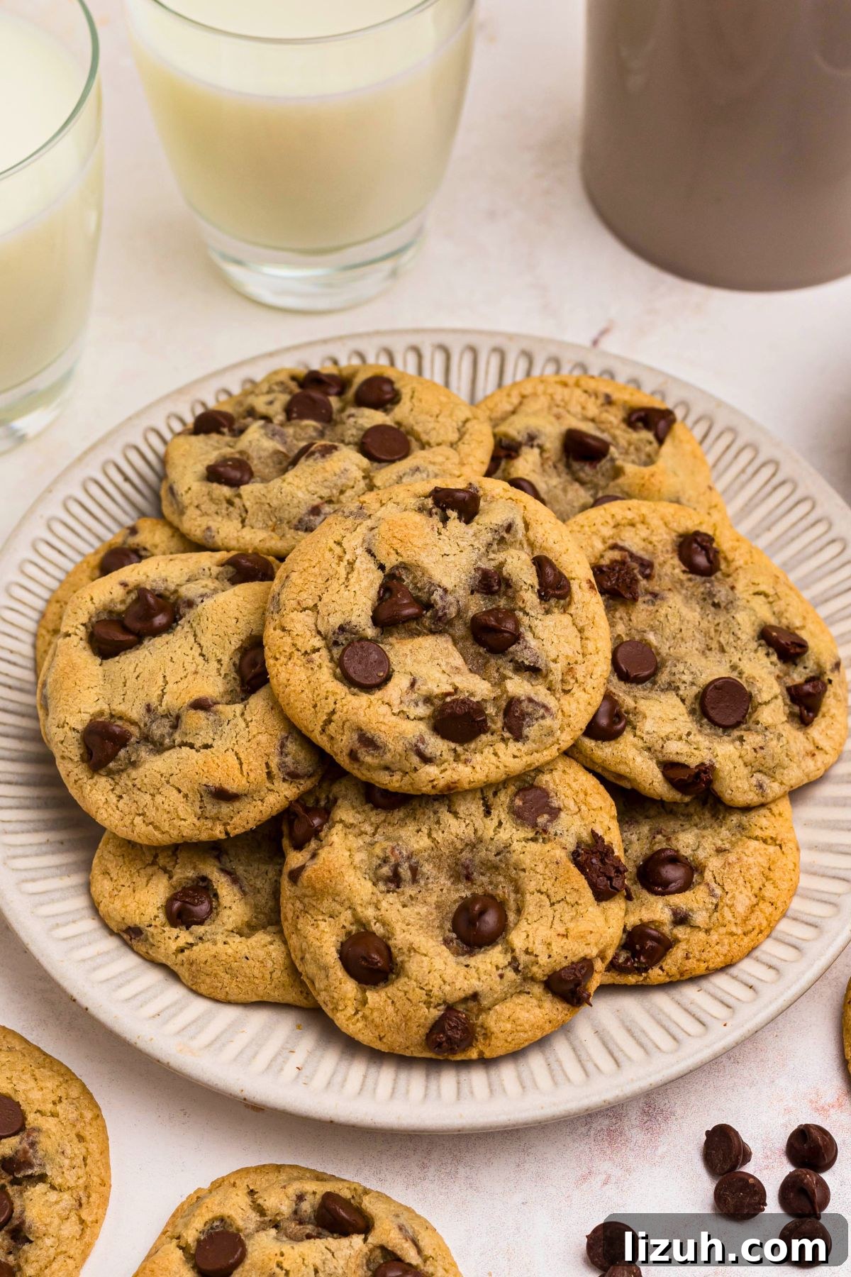 Golden brown chocolate chip cookies stacked on a white plate with chocolate chips on the table. 