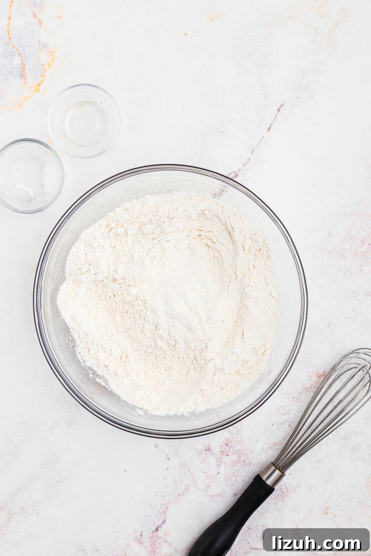 Flour and other ingredients mixed in a clear glass bowl. 