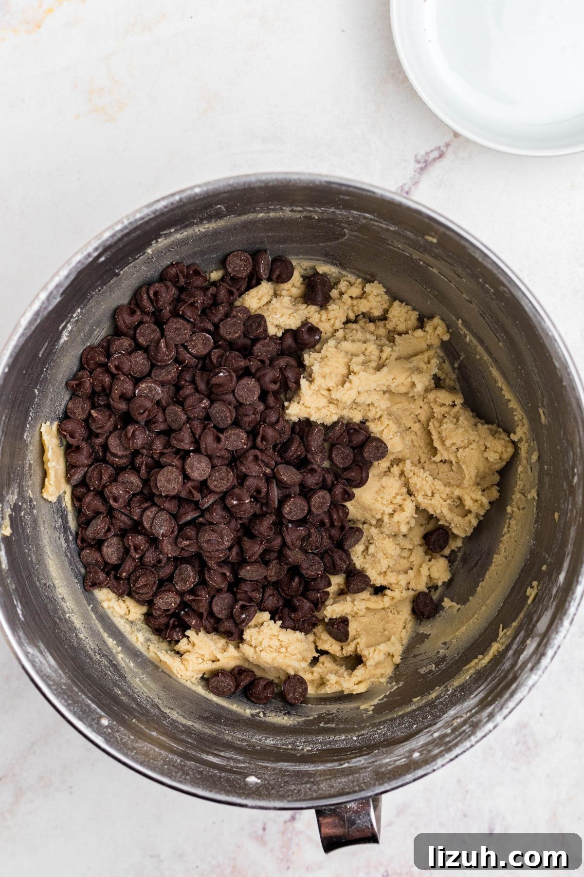 Soft dough in a mixing bowl with chocolate chips being added. 