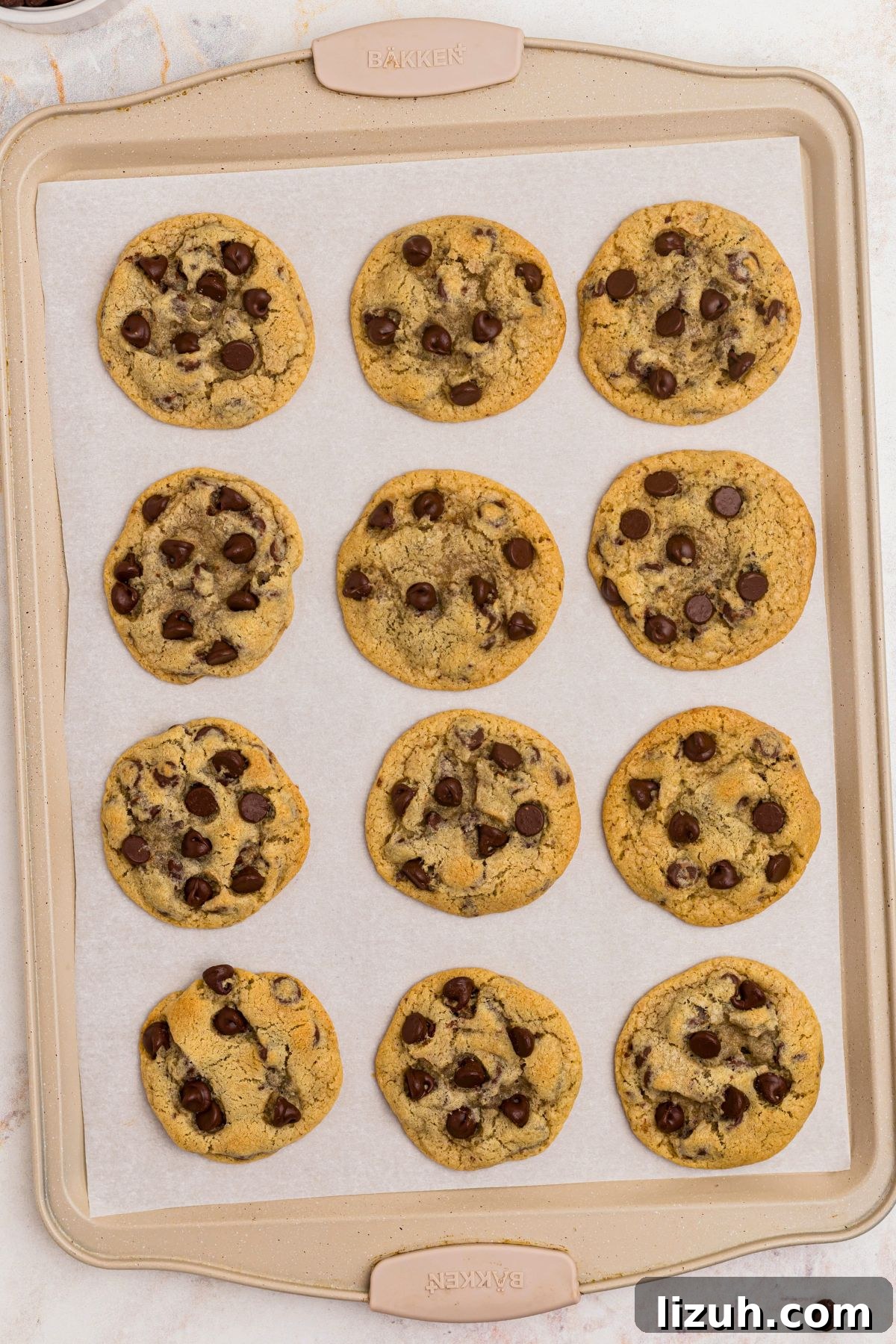 Golden baked chocolate chip cookies on a baking sheet lined with parchment paper. 