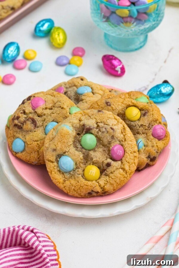 Golden chocolate chip cookies with pastel candies on plates, in front of candy dish and glasses of milk.