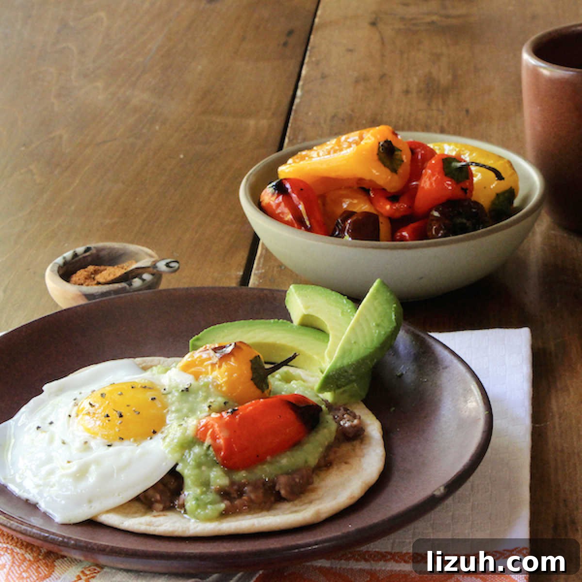 April Vegetarian Meal Plan: Week 4 Recipes & Grocery List 11 Huevos Rancheros on a plate with roasted mini peppers in a bowl beside it.
