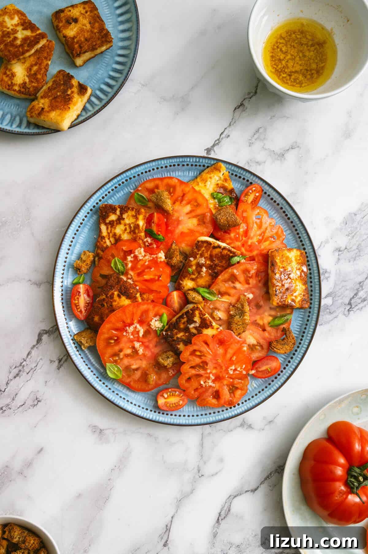 Table setting with a platter of tomato and halloumi salad, fried cheese slices, and garlic dressing.