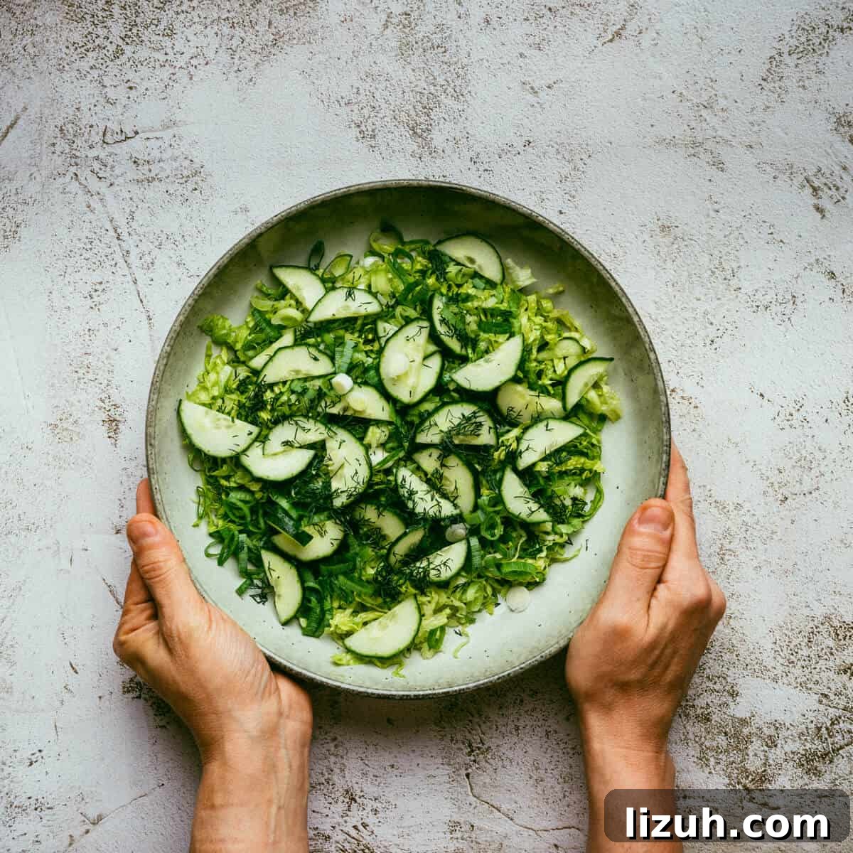 two hands holding a bowl filled with salad greens.