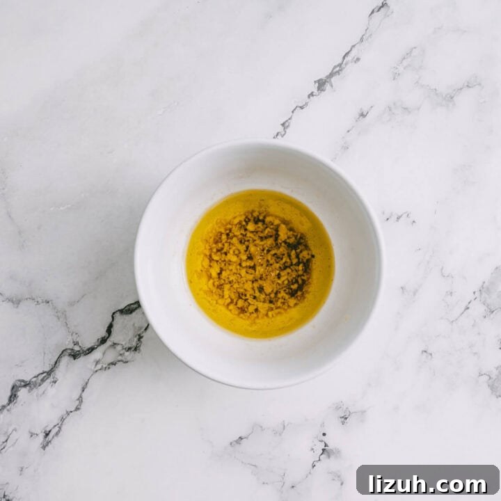 White bowl with garlic and olive oil dressing for tomato and halloumi salad on a marble background.