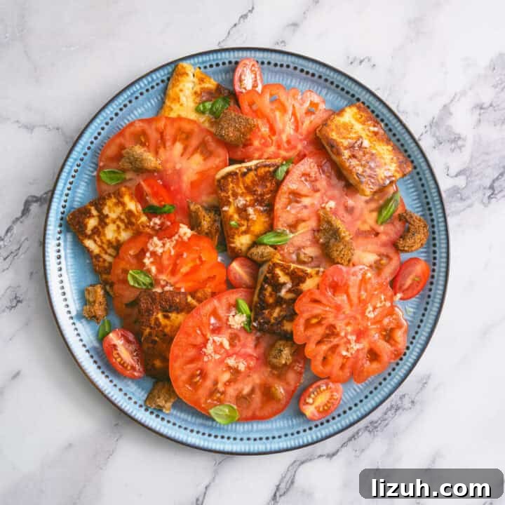 Blue plate with tomato and halloumi salad, topped with croutons and fresh basil.