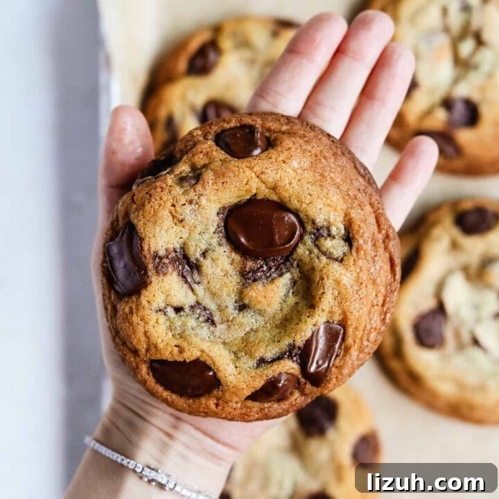 Hand holding a giant bakery-style chocolate chip cookie with crispy edges and a chewy center.