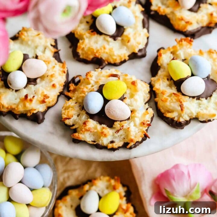 Chocolate-covered coconut macaroon nests with Cadbury mini eggs arranged on a marble platter with light and dark pink ranunculus flowers.