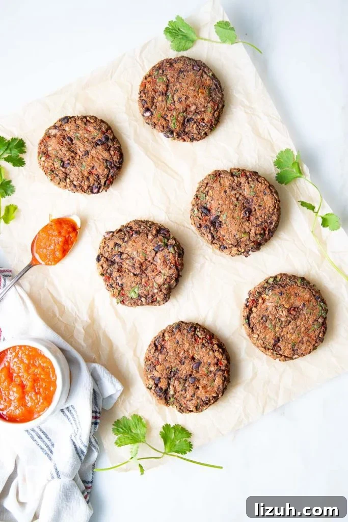 Black Bean Veggie Burger Recipe — Flavorful Homemade Patties 2 Parchment paper with veggie burgers and a bowl of red sauce to spoon on top.