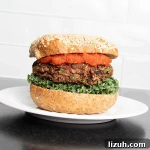 Black Bean Veggie Burger Recipe — Flavorful Homemade Patties 14 Veggie burger with red sauce, lettuce and a sesame bun on a plate.