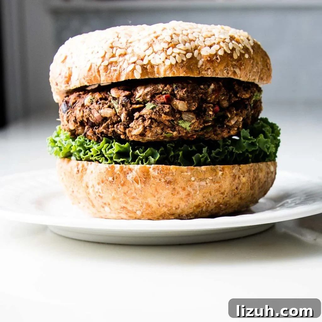 Black Bean Veggie Burger Recipe — Flavorful Homemade Patties 3 White plate with a burger in sesame seed bun on top of lettuce.