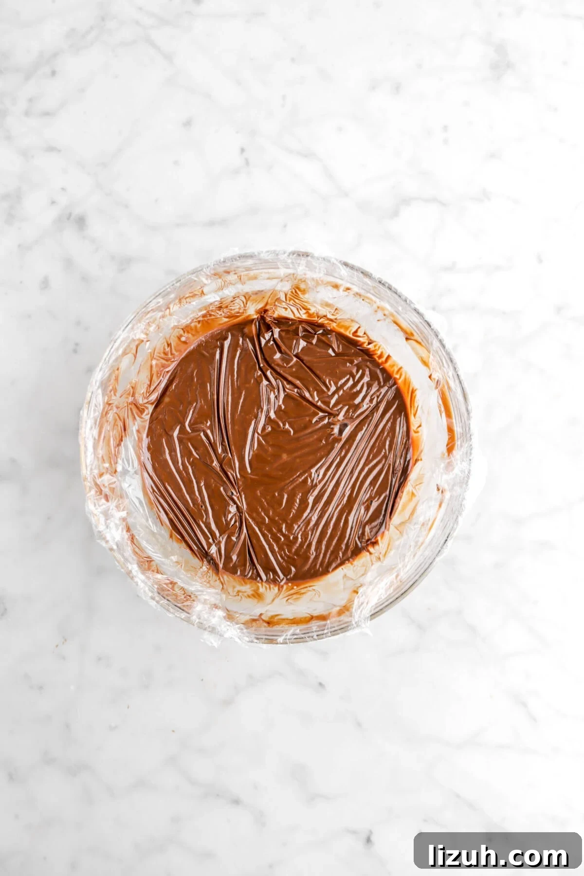 plastic wrap over ganache in glass bowl on marble surface