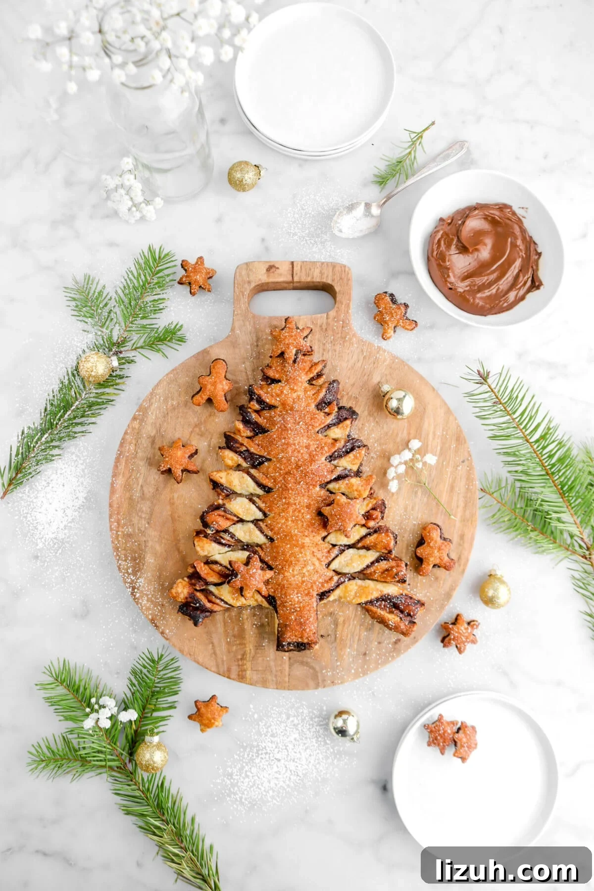 christmas tree tear and share on circle wood board with pine branches, bowl of ganache, gold ornaments, and gingerbread men and snowflake shaped puff pastry bites around.