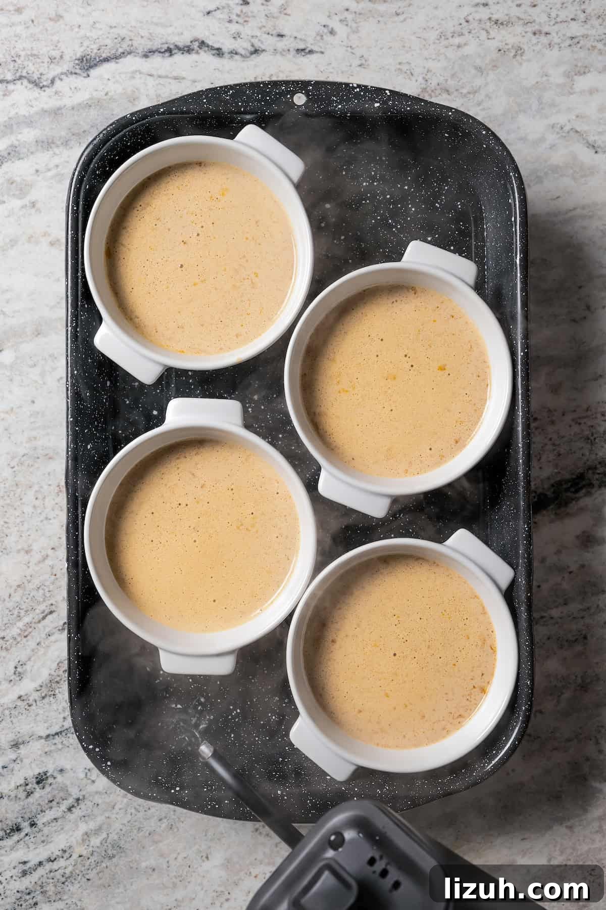Ramekins filled with coffee crème brûlée batter on a baking sheet.