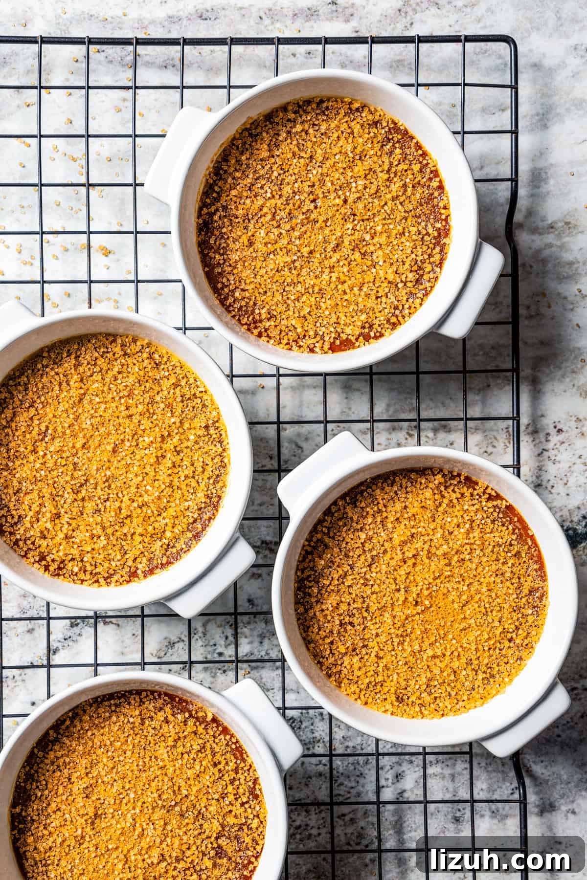 Coffee crème brûlée topped with sugar in ramekins cooling on a wire rack.