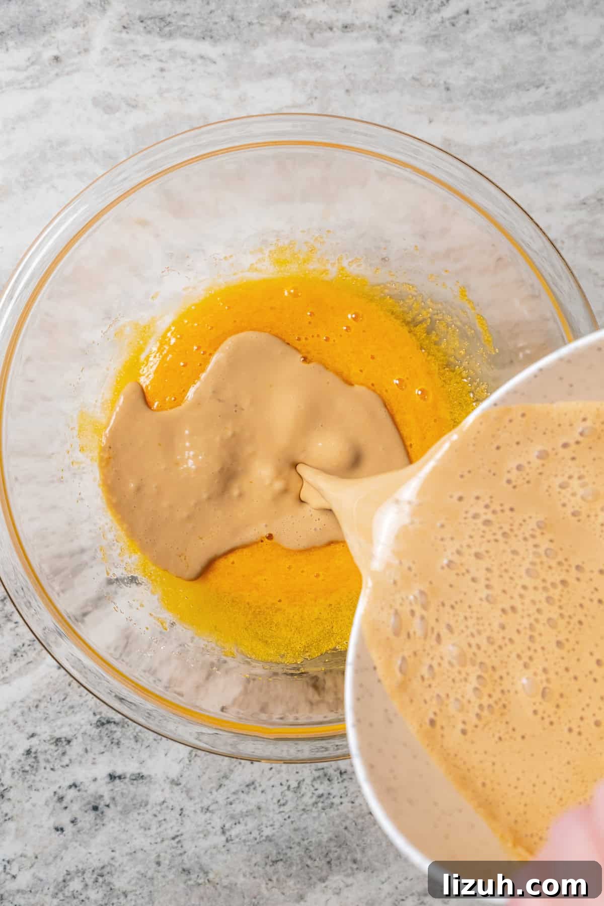 Coffee caramel mixture being poured into the egg yolks and sugar in a bowl.