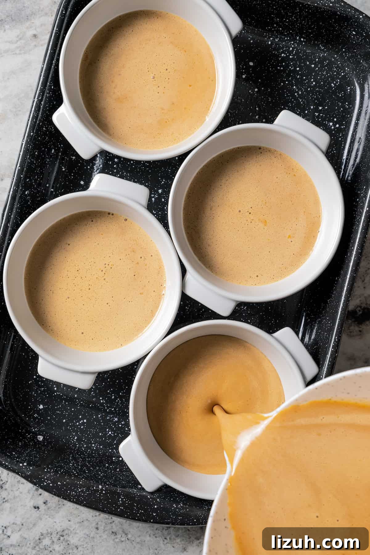 Coffee crème brûlée batter being poured into ramekins on a baking sheet.