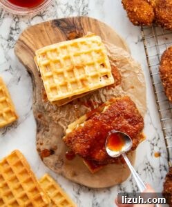 cornflake chicken waffle sandwich overhead shot of two cornflake fried chicken sandwiches with hand pouring syrup over one of them