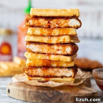 4 cornflake fried chicken waffle sandwiches stacked on each other on wooden board with sriracha maple dripping down
