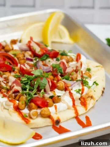¾ view of a sheet pan with Falafel-Spiced Chickpea Flatbread on top surrounded by garnishes.