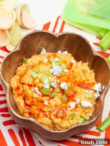 Bowl of buffalo chickpea dip with celery sticks and veggie chips