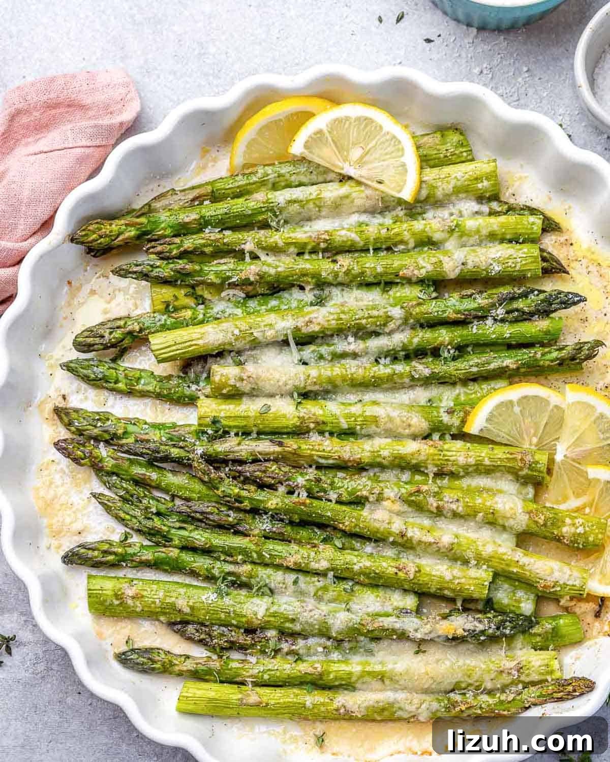 Crispy Parmesan-Roasted Asparagus — Oven-Baked Recipe 2 baked asparagus in a dish topped with parmesan cheese and lemon garnishes.