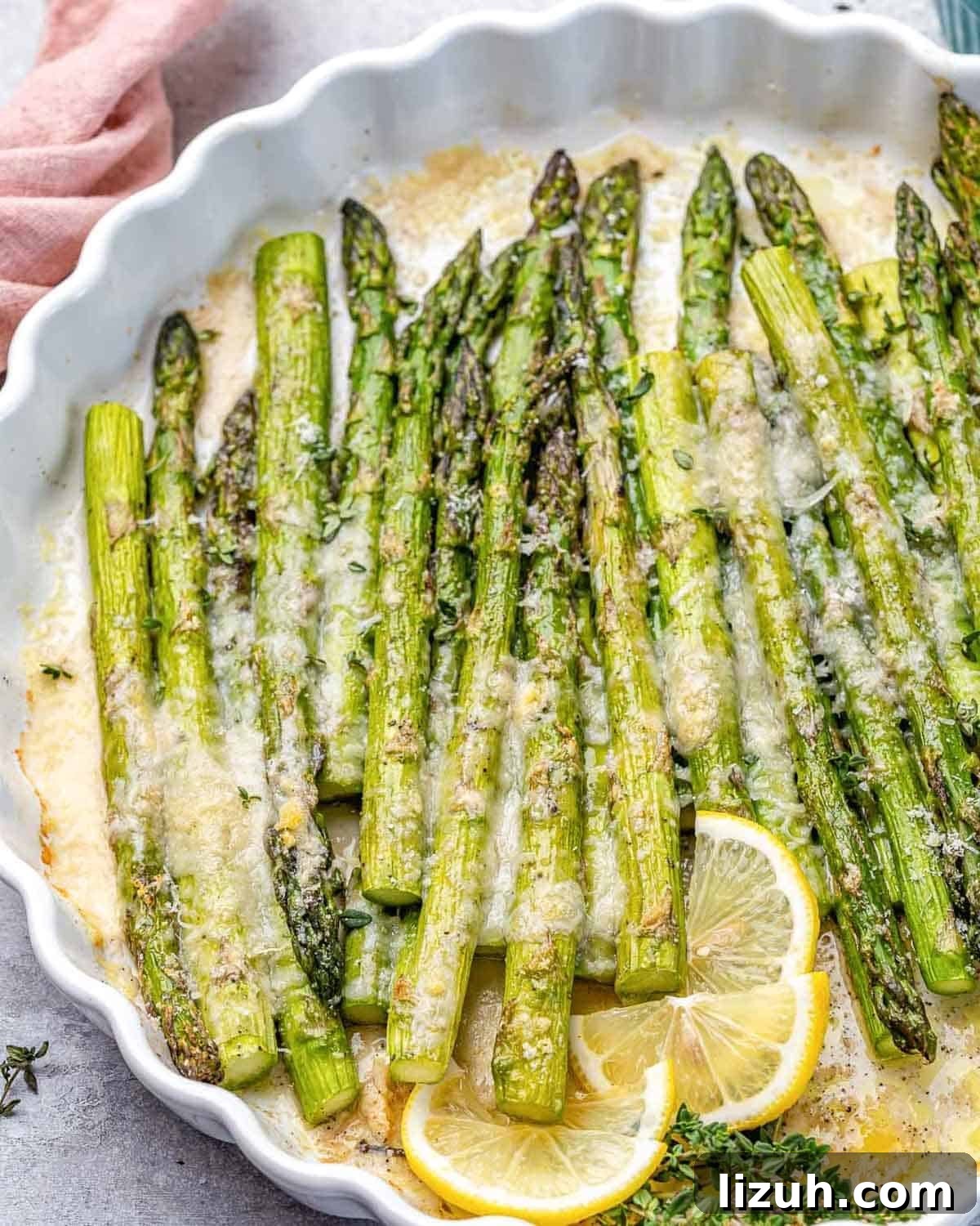 Crispy Parmesan-Roasted Asparagus — Oven-Baked Recipe 6 a dish with baked asparagus topped with parmesan cheese and lemon garnish.