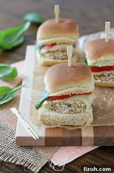 Simple and easy crispy eggplant sliders! Lightly breaded eggplant rounds topped with juicy tomato, mozzarella and fresh basil. Perfect for the summer! Three Crispy Eggplant Sliders on a wood cutting board.