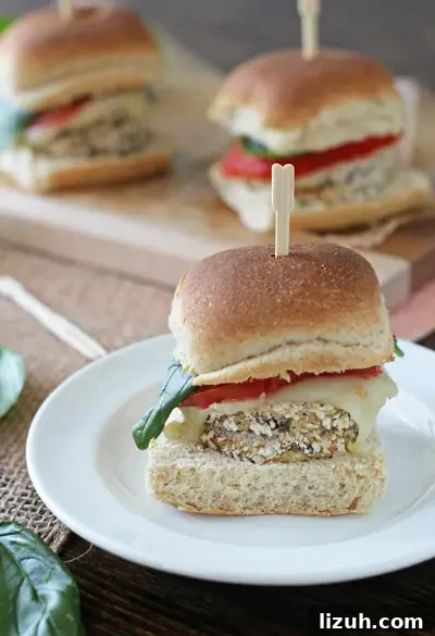 Simple and easy crispy eggplant sliders! Lightly breaded eggplant rounds topped with juicy tomato, mozzarella and fresh basil. Perfect for the summer! An Eggplant Slider on a white plate with more in the background.
