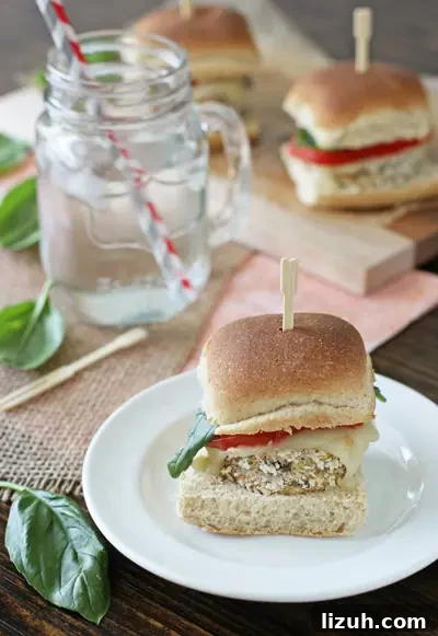 Simple and easy crispy eggplant sliders! Lightly breaded eggplant rounds topped with juicy tomato, mozzarella and fresh basil. Perfect for the summer! An Eggplant Slider on a white plate with a glass of water to the side.