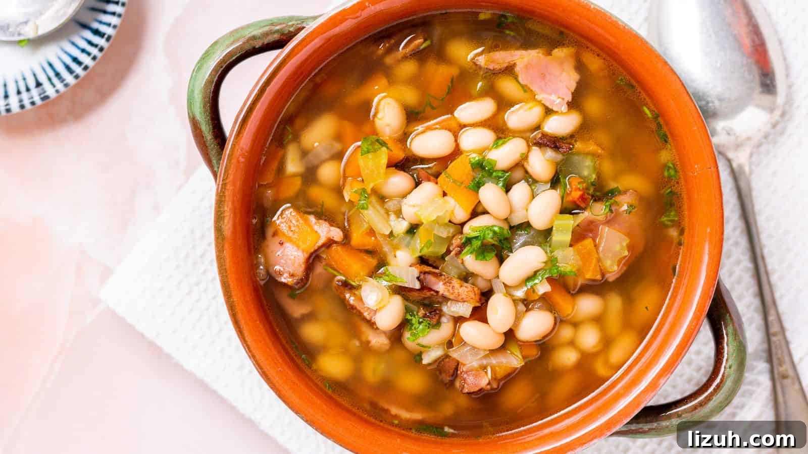 A bowl of bean soup with chunks of ham and diced vegetables, served in a rustic terracotta bowl with a spoon on the side.