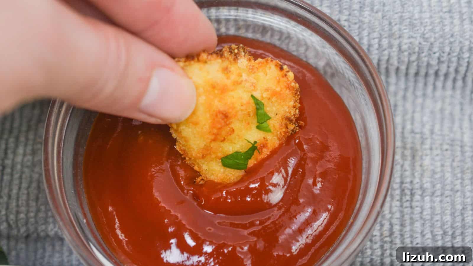 Hand dipping a chicken nugget into a bowl of ketchup, with a gray cloth background.