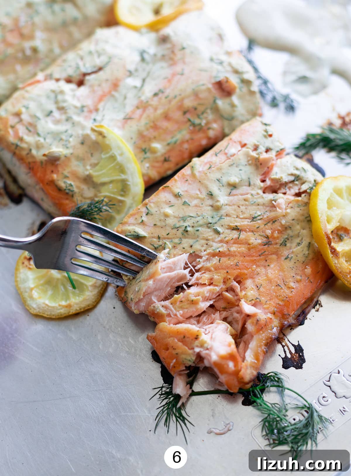 Baked salmon with dill sauce on a sheet pan, getting cut into by a fork. 