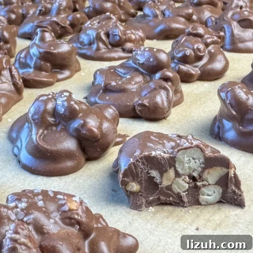Close up of homemade chocolate covered cashew cluster on parchment paper with a bite out of one show the meaty nuts inside.