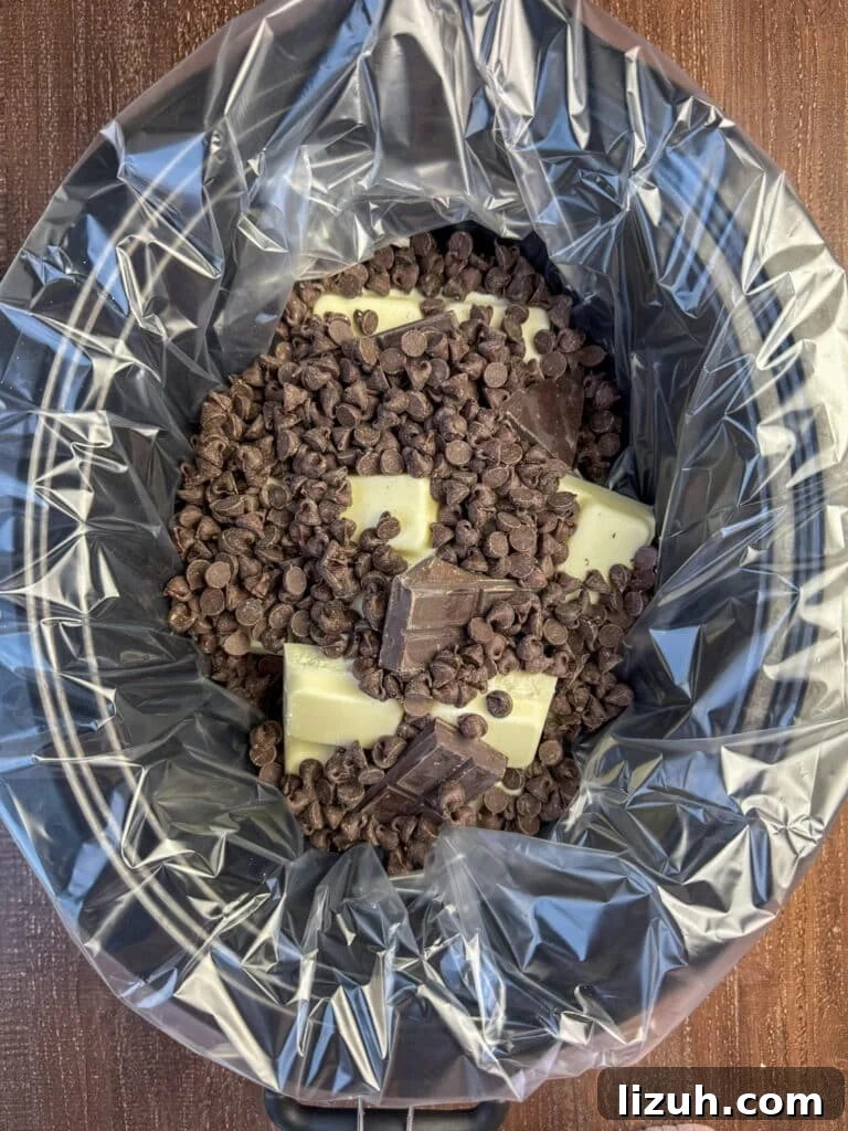 Semi sweet chocolate chips poured over almond bark and German sweet chocolate in a lined crock pot.