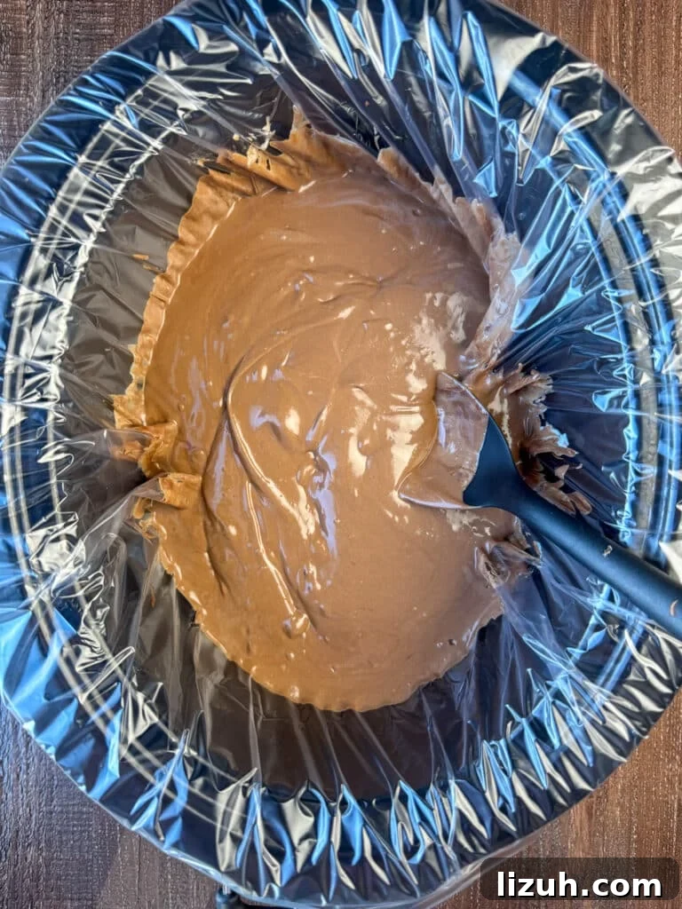 Spoon stirring smooth melted milk chocolate in a large black slow cooker.