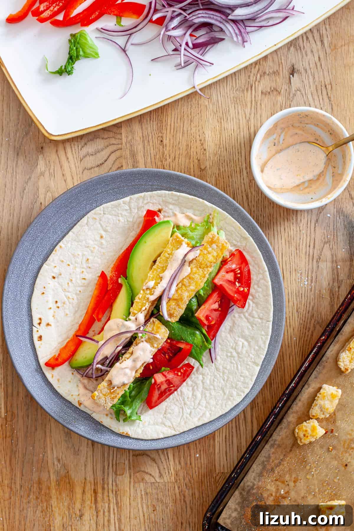 Crispy Buffalo Tofu Wraps with Cooling Ranch Slaw 2 A plate with crispy buffalo tofu wrap topped with avocado, red peppers, lettuce, red onions and a homemade buffalo ranch sauce.