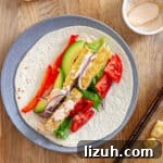A plate with crispy buffalo tofu wrap topped with avocado, red peppers, lettuce, red onions and a homemade buffalo ranch sauce.