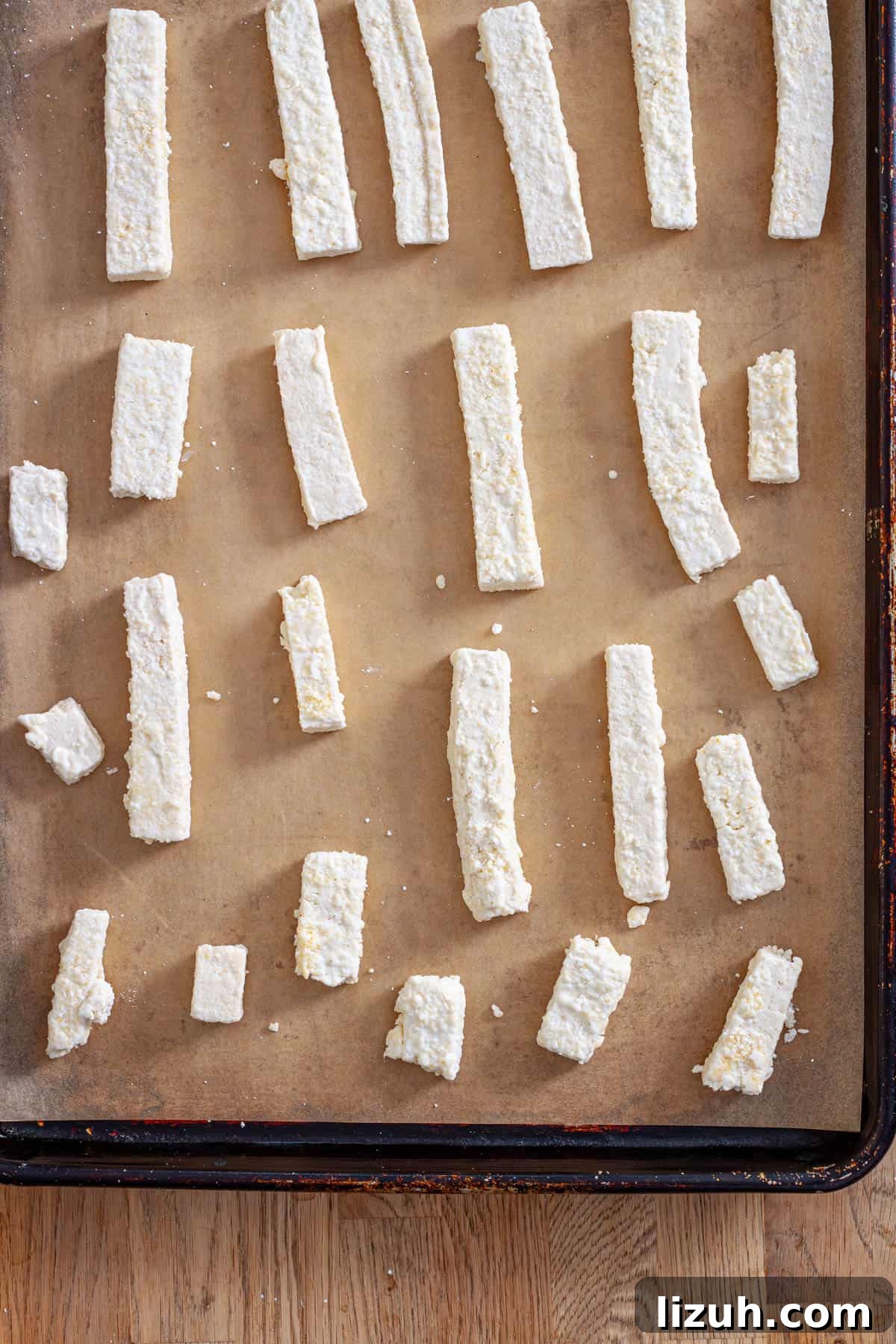Crispy Buffalo Tofu Wraps with Cooling Ranch Slaw 6 Strips of tofu coated in cornstarch on a parchment-lined baking sheet.