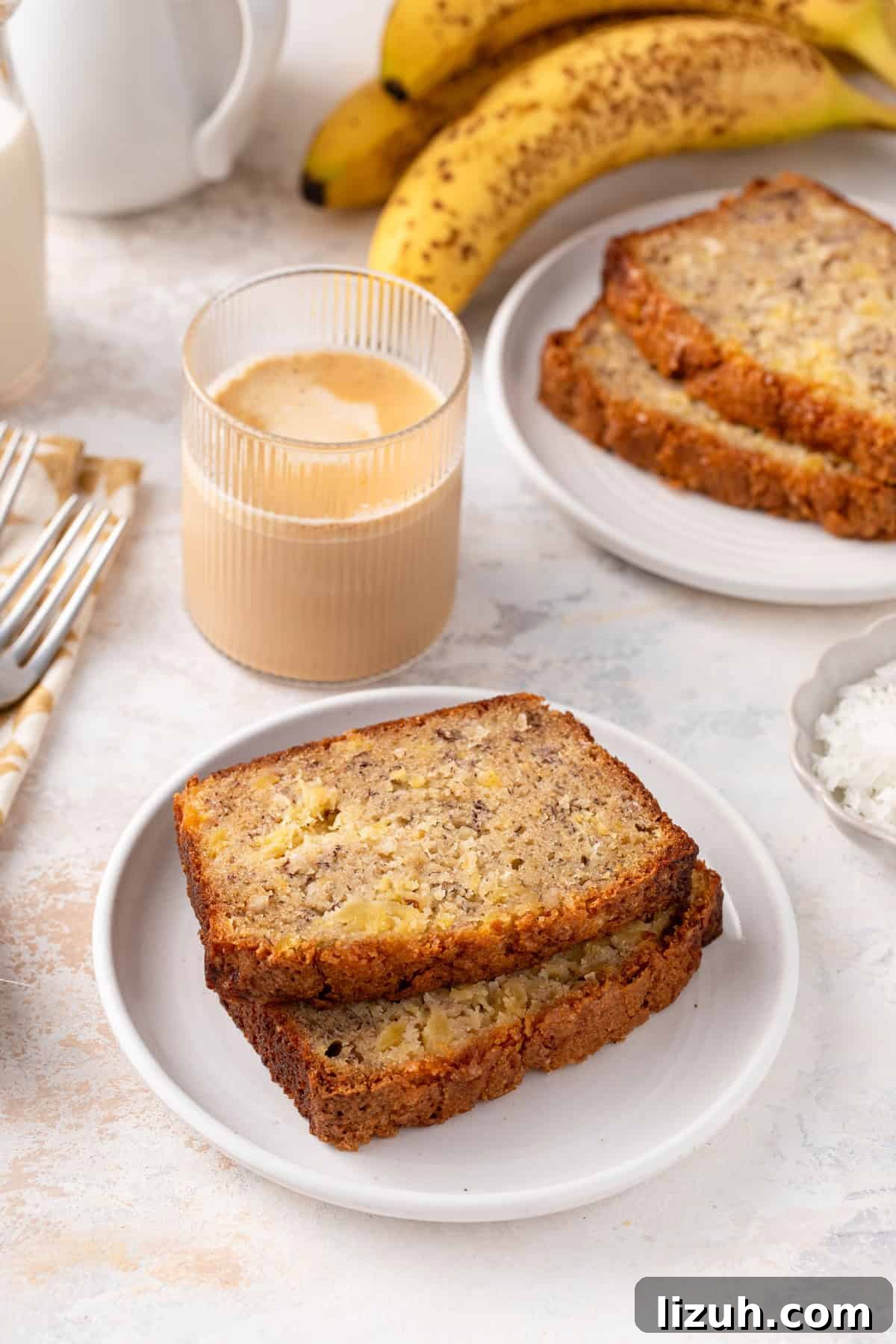Two slices of pineapple banana bread on a white plate next to an iced coffee.