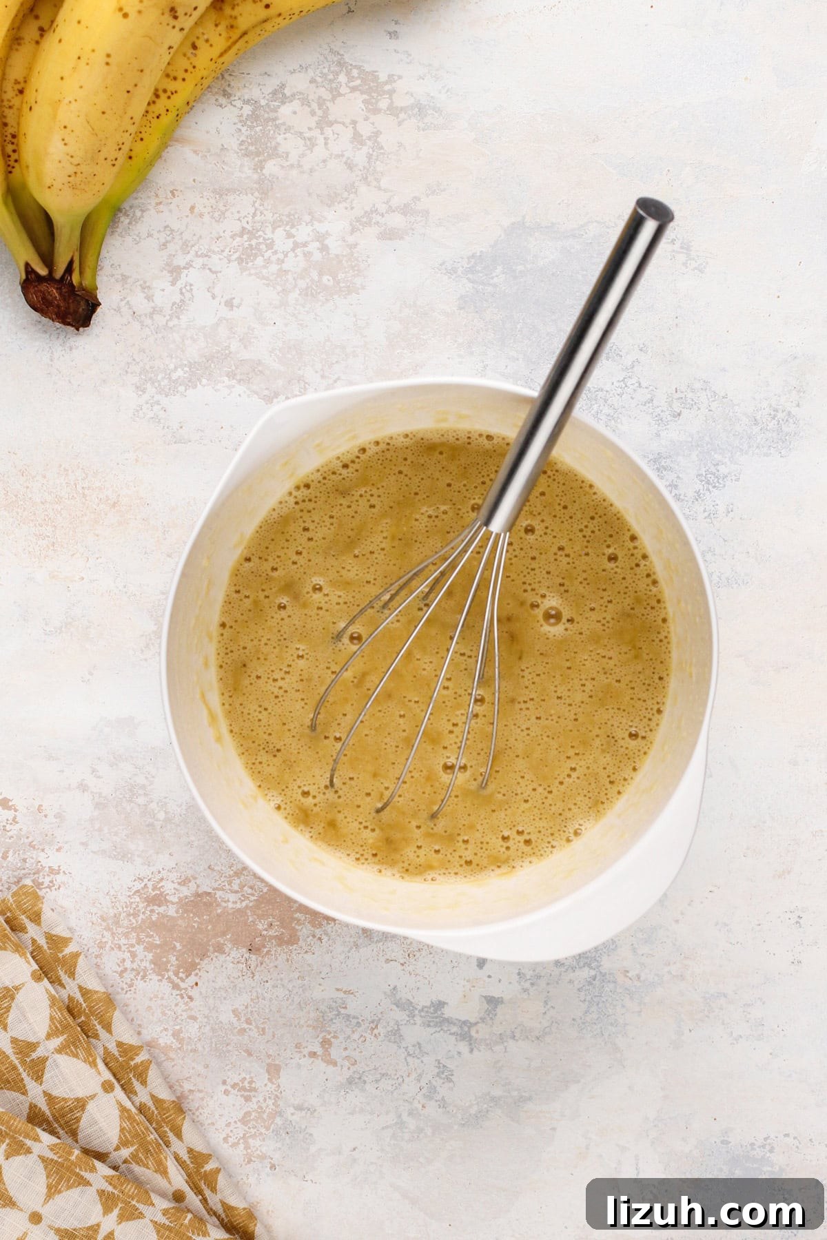 Wet ingredients for pineapple banana bread whisked together in a white bowl.
