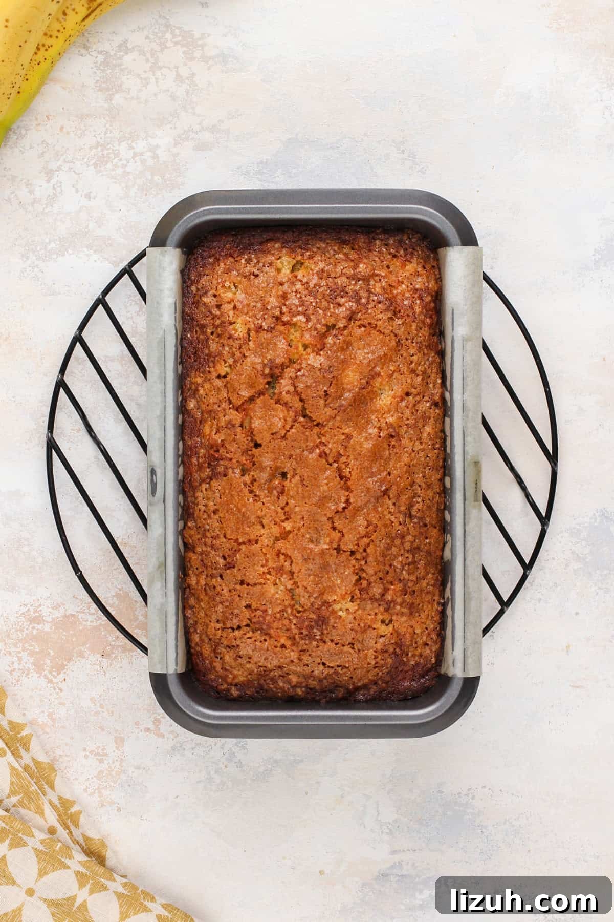Baked loaf of pineapple banana bread in a loaf pan on a wire rack.