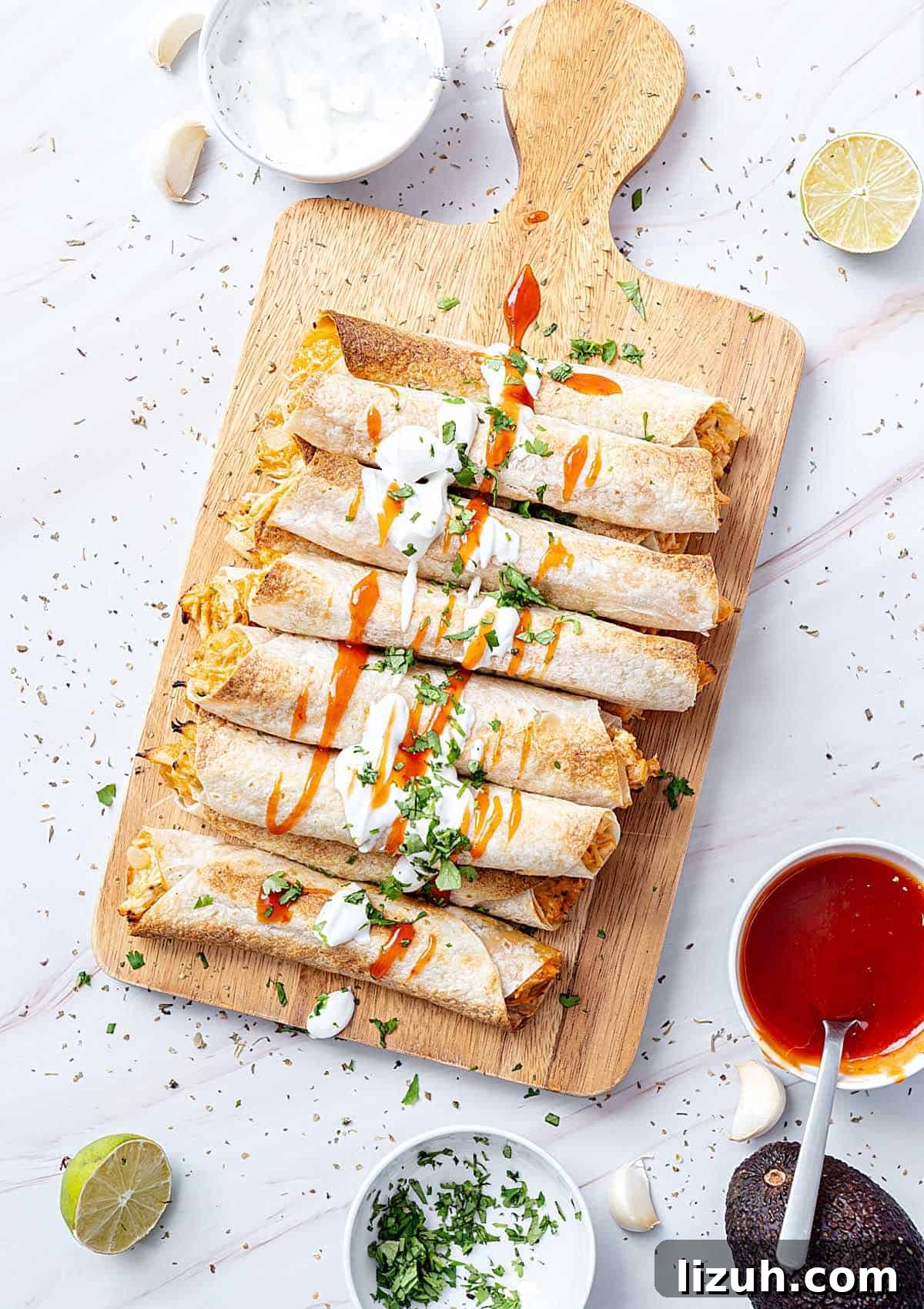 Crispy Baked Chicken Taquitos Recipe for a Flavorful Dinner 2 White marbled surface with wooden board and chicken taquitos. Bowls with sauce and cream. Top view.