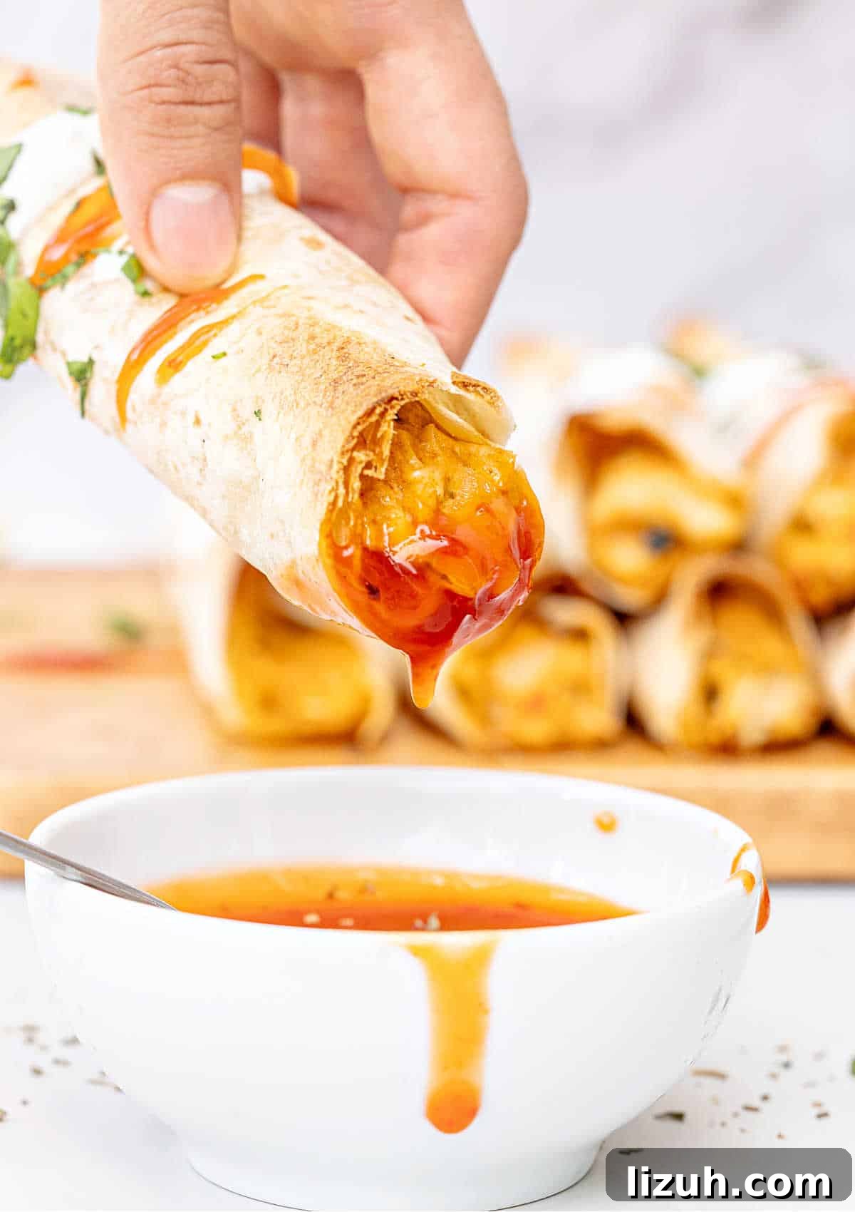 Crispy Baked Chicken Taquitos Recipe for a Flavorful Dinner 3 Dipped baked taquito in a white bowl with sauce. Taquitos in the marbled background.