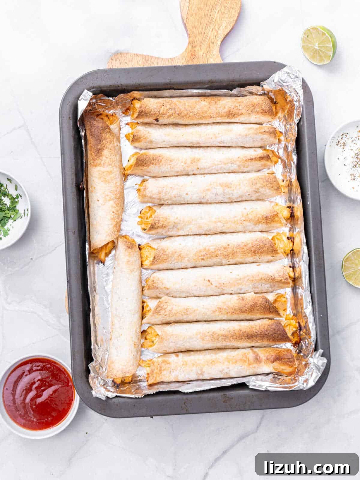 Crispy Baked Chicken Taquitos Recipe for a Flavorful Dinner 6 Oven tray with baked taquitos. White marbled surface, bowls with garnishes.